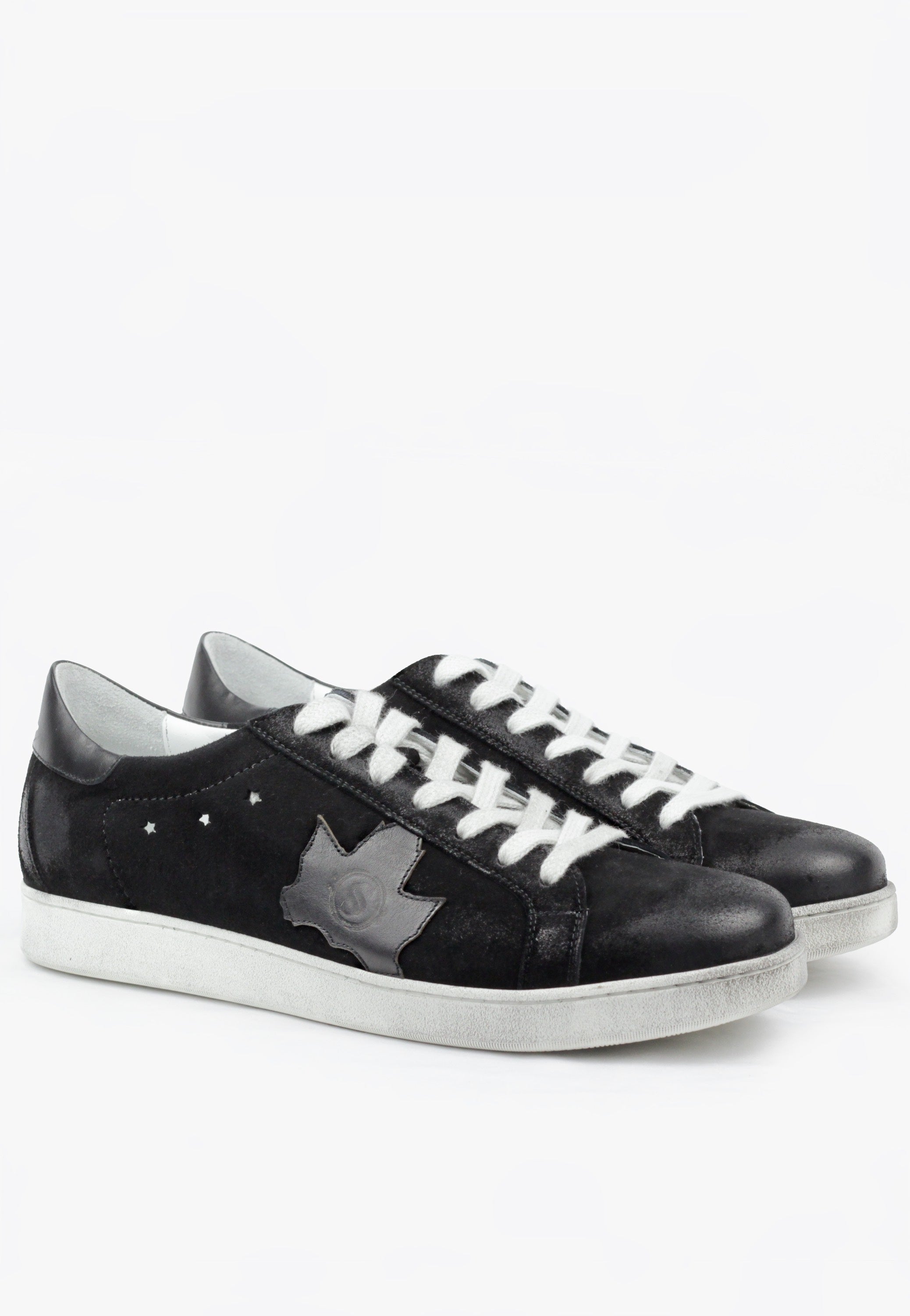 A pair of black suede sneakers with white laces and a subtle distressed finish. The sneakers feature a detailed leaf-shaped logo in a contrasting white color.